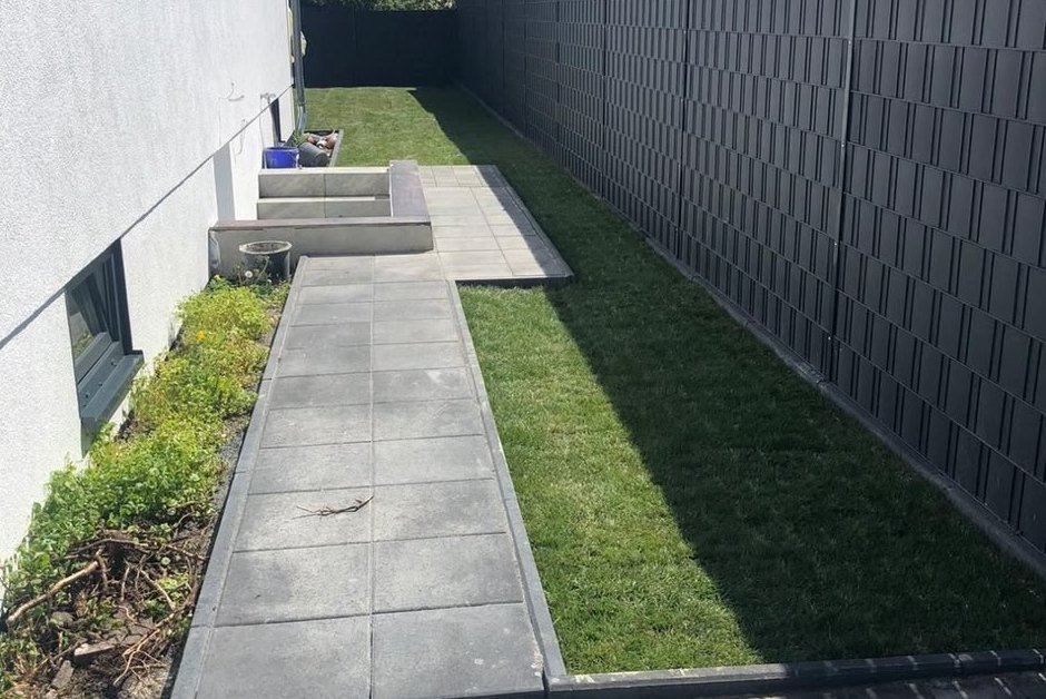 Gartenweg am Haus nach den Arbeiten: Fertiger Plattenweg mit Rasenstreifen entlang des Sichtschutzzauns
